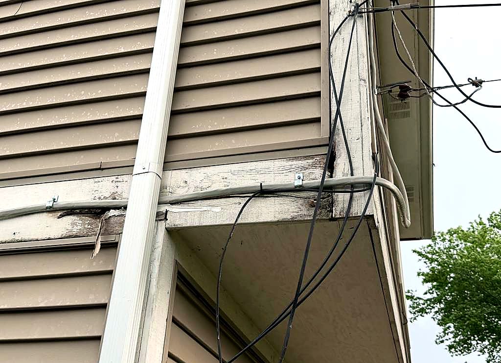Rotted fascia board and loose wiring at the roofline