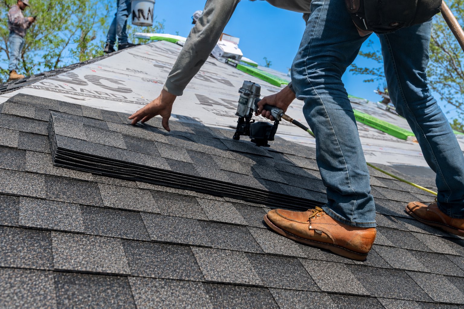 Roofer nail-gunning architectural shingle into place, close angle